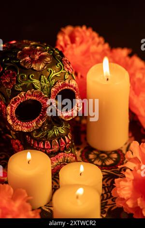 Un primo piano verticale di un cranio decorato adornato con fiori metallici, circondato da vibranti calendule arancioni e candele accese. La configurazione si basa su una D. Foto Stock