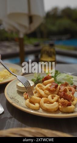 Primo piano di calamari e insalata di bacon su un piatto con un bicchiere di vino a bordo piscina. Foto Stock