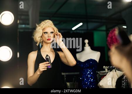 Una drag queen in un abito nero prepara il backstage fissando i capelli con una lacca. Foto Stock