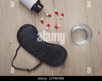 Maschera per occhi neri accanto a un bicchiere d'acqua e sonniferi su un tavolo. Concetto di insonnia. Foto Stock