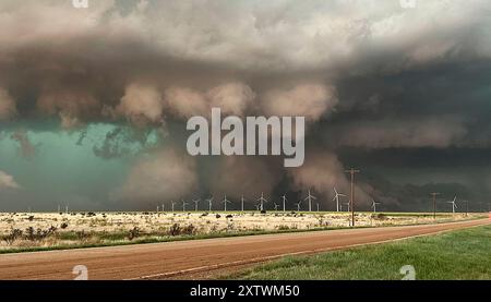 Un minaccioso tornado si forma sopra un parco eolico con nuvole di tempesta scure che incombono nel cielo, come si vede da una prospettiva a lato della strada. Foto Stock