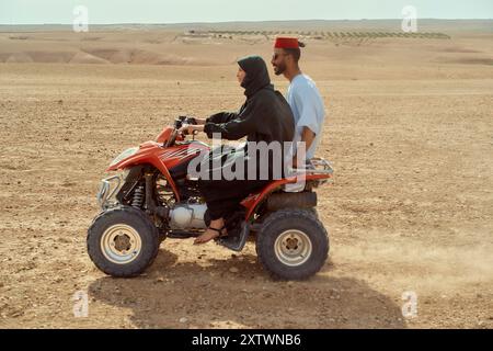 Due persone in sella a un quad in un paesaggio desertico, con l'autista che indossa abiti tradizionali. Foto Stock