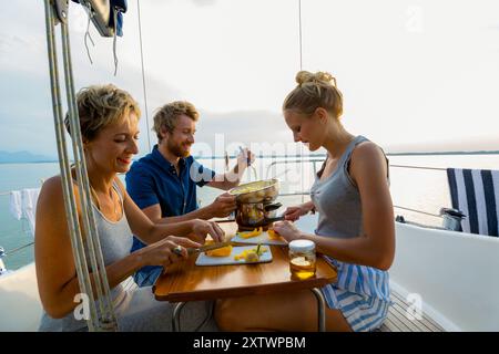 Gli amici potranno gustare un pasto insieme su una barca a vela al tramonto con una vista pittoresca dell'acqua. Foto Stock