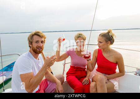 Tre amici si godranno un drink e si divertiranno su una barca con un lago panoramico sullo sfondo durante il tramonto. Foto Stock