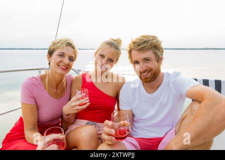 Tre amici si godono un drink su una barca con un lago sullo sfondo. Foto Stock