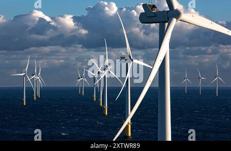 Le turbine eoliche offshore si ergono alte sopra l'oceano con un cielo blu nuvoloso sullo sfondo. Foto Stock