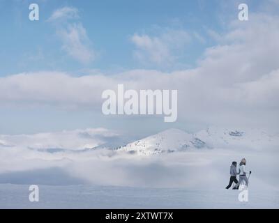 Due persone godono di un paesaggio innevato sulle montagne mentre sciano di fondo sotto un cielo blu con nuvole soffici. Foto Stock