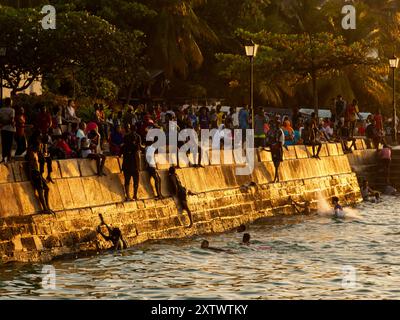 Città di pietra, Zanzibar, Tanzania - Jan 2021: Folla della gente sui giardini di Forodhani e bambini che saltano in acqua da un muro durante il tramonto. C Foto Stock