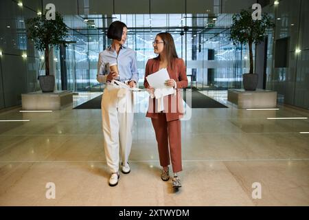 Due colleghi, uno con una gamba protesica, camminano e chiacchierano in una moderna hall dell'ufficio. Foto Stock