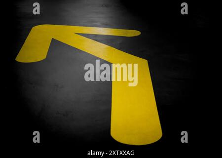 Freccia gialla su una superficie di asfalto scuro, rivolta verso l'angolo superiore sinistro, che indica le direzioni Foto Stock