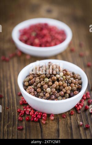 Grani di pepe rosa freschi (conservati) su un vecchio e rustico tavolo in legno, messa a fuoco selettiva, foto ravvicinata Foto Stock