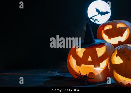 Tre zucche scolpite impilate con illuminazione a candela per la decorazione di Halloween su sfondo scuro con luna piena Foto Stock