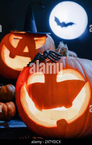 Zucche di Halloween scolpite che brillano al buio, ragni spaventosi, sfondo scuro con luna piena e silhouette di pipistrello Foto Stock