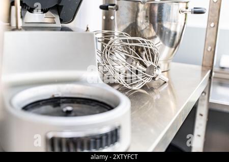 Primo piano di un mixer e delle fruste su un tavolo di produzione della cucina in acciaio. Negozio di dolciumi. Locali di produzione dolciaria. Foto di alta qualità Foto Stock