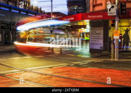 Sydney, Australia - 20 giugno 2024: Angolo di strada nel centro di Parramatta al tramonto con la nuova linea del tram della metropolitana leggera sfocato a lunga esposizione. Foto Stock