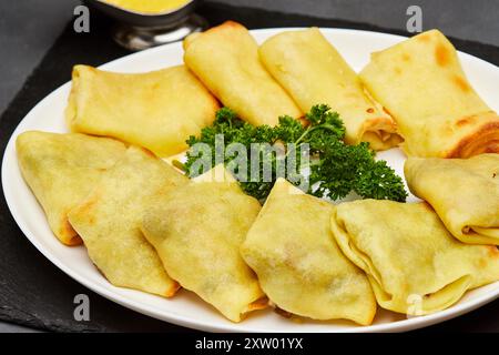 Crepe dorate ripiene di ripieno saporito, servite con prezzemolo fresco su un piatto bianco Foto Stock