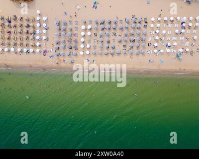 Video con drone che cattura una vista dall'alto verso il basso di una spiaggia con file di ombrelloni colorati allineati perfettamente sulla sabbia accanto al litorale. Il vibrante Foto Stock
