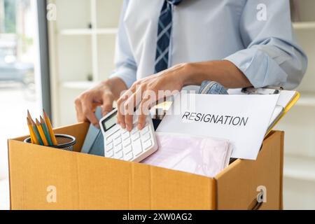 Triste giovane uomo d'affari che mette la sua roba in una scatola prima di lasciare il suo ufficio dopo le sue dimissioni Foto Stock