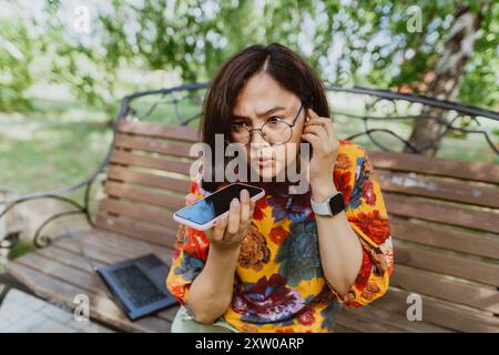 Una donna scontenta che conversava con rabbia al telefono in una giornata di sole nel parco. Sconvolge l'imprenditore con i dispositivi digitali, impegnato con fermezza in un rumoroso pho Foto Stock