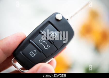 Una vista dettagliata del telecomando della chiave del veicolo con pulsanti di blocco, sblocco e sbloccaggio del vano bagagli. La mano regge delicatamente il telecomando contro un bac colorato sfocato Foto Stock