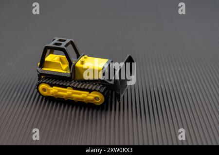 Primo piano del Bulldozer giocattolo giallo su superficie nera Foto Stock