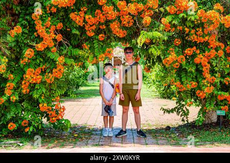 I fratelli posano sotto un arco floreale arancione nei giardini botanici di Penang a George Town, Penang, Malesia Foto Stock