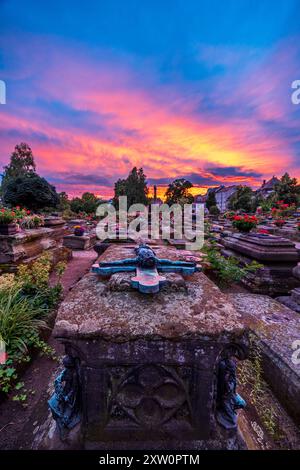 Nürnberger Stadtbild Der Johannisfriedhof a Nürnberg bei Sonnenuntergang. Im Vordergrund steht ein altes Grab mit einem verwitterten Grabkreuz, das den gekreuzigten Jesus zeigt. Der Himmel ist in kräftigen Orange- und Violetttönen gefärbt. Die Gräber sind mit Blumen geschmückt. Nürnberg Bayern Deutschland *** paesaggio urbano di Norimberga Cimitero di San Giovanni a Norimberga al tramonto in primo piano è una vecchia tomba con una croce intemprata che mostra il Gesù crocifisso il cielo è colorato in forti tonalità di arancione e viola le tombe sono decorate con fiori Norimberga Baviera Germania 20240712-6V2A5179-HDR-M4 Foto Stock