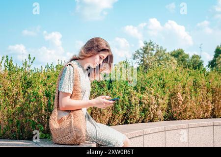 Giovane bella ragazza in abito verde seduta e con lo smartphone fuori. Foto Stock