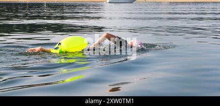 Primo piano di una nuotatrice che nuota in mare aperto indossando una muta corta e una galleggiante verde neon per la sicurezza. Foto Stock