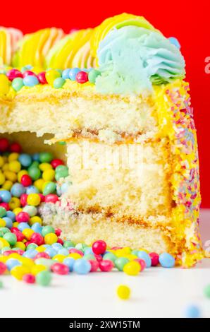 Una torta con spruzzette colorate e un buco nel mezzo. La torta viene tagliata in modo da rivelare un ripieno colorato Foto Stock