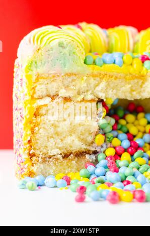 Una torta con spruzzette colorate e un buco nel mezzo. La torta viene tagliata in modo da rivelare un ripieno colorato Foto Stock