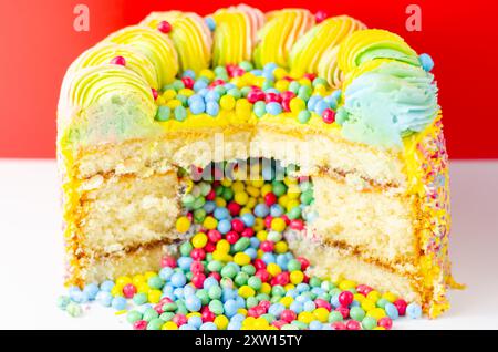 Una torta con spruzzette colorate e un buco nel mezzo. La torta viene tagliata in modo da rivelare un ripieno colorato Foto Stock