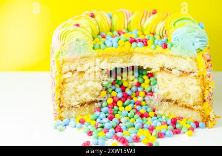 Una torta con spruzzette colorate e un buco nel mezzo. La torta viene tagliata in modo da rivelare un ripieno colorato Foto Stock