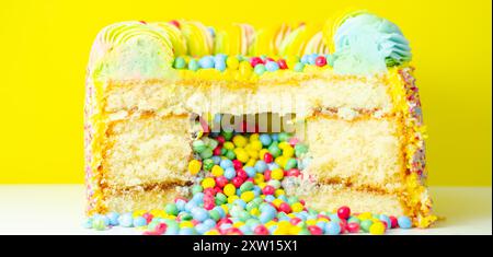 Una torta con spruzzette colorate e un buco nel mezzo. La torta viene tagliata in modo da rivelare un ripieno colorato Foto Stock