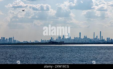 Nuvoloso, nebbioso, skyline di New York nel tardo pomeriggio, visto da Ferry Point/Throggs Neck, Bronx, con Rikers Island (prigione) in primo piano. Foto Stock