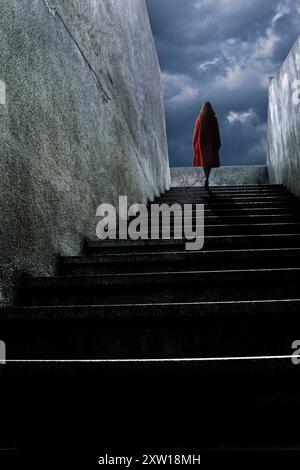 donna con cappotto rosso che sale su una scala Foto Stock