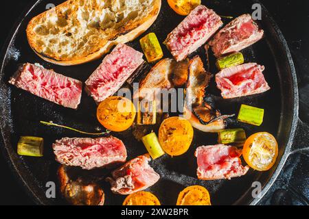 Il tonno viene scottato in una padella di ghisa con pomodori ciliegini, asparagi, pancetta e pane tostato. Foto di alta qualità Foto Stock