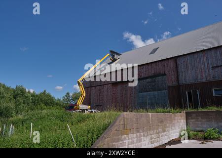 Riparazione di un tetto piatto di un edificio agricolo con ascensore giallo in una soleggiata giornata estiva a Skaraborg in Svezia Foto Stock