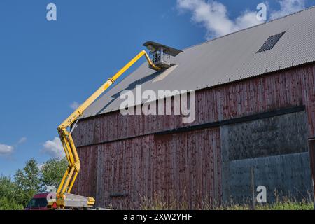 Riparazione di un tetto piatto di un edificio agricolo con ascensore giallo in una soleggiata giornata estiva a Skaraborg in Svezia Foto Stock