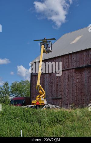 Riparazione di un tetto piatto di un edificio agricolo con ascensore giallo in una soleggiata giornata estiva a Skaraborg in Svezia Foto Stock