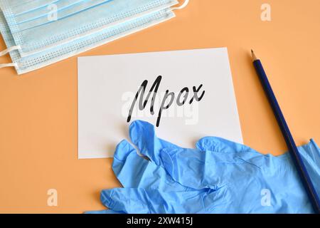 Maschere di protezione e guanti chirurgici blu con carta bianca e testo Mpox. Concetto per Mpox virus. Foto Stock