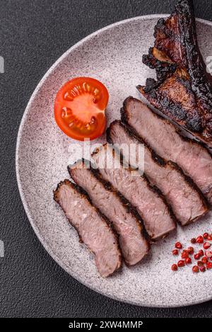 Succulenta bistecca di manzo alla griglia con sale, spezie ed erbe aromatiche su sfondo di cemento scuro Foto Stock