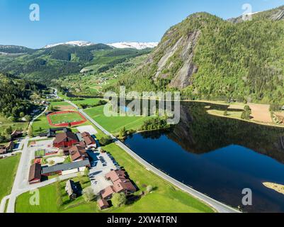 Veduta aerea del fiume Otra nel villaggio Valle, riflessi di ripide montagne nel fiume calmo, centro scolastico e campo sportivo locale, valle Setesdal, Foto Stock