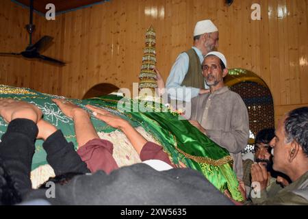 Srinagar, India. 17 agosto 2024. Gli uomini musulmani del Kashmir toccano la sacra tomba di Hazrat Sultan Sayed Muhammad 'Ali 'Ala Balkhi durante la cerimonia Poshakbandi a Pakherpora, che si trova a 43 chilometri da Srinagar, Kashmir, India, il 17 agosto 2024. Secondo la tradizione locale, Hazrat Sultan Sayed Muhammad 'Ali 'Ala Balkhi era ritenuto un discendente del profeta Maometto e governava la città di Millahin Balkh, che si trova nell'attuale Afghanistan. (Foto di Danish Showkat/Sipa USA.) Crediti: SIPA USA/Alamy Live News Foto Stock