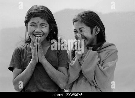 Due sorelle ridono salutano Namaste sulle colline centrali del Nepal durante il trekking al Santuario dell'Annapurna - Nepal 1988 Foto Stock