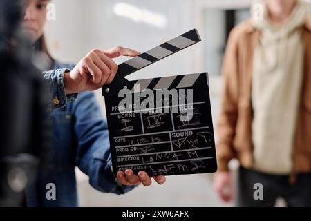 Membro della troupe che tiene in mano il clapper mentre si prepara una scena cinematografica su un set cinematografico. Lo sfondo sfocato include un altro membro della troupe che aggiunge profondità alla scena di produzione cinematografica Foto Stock