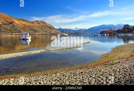 Il lago Wanaka e barche con il Sud delle Alpi in background. Central Otago, Nuova Zelanda. In primo piano nota come basso il livello del lago è dopo uno Foto Stock