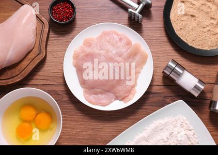 Fare schnitzel. Carne cruda, spezie, tuorli, briciole di pane e tenderizer su tavola di legno, piatti Foto Stock