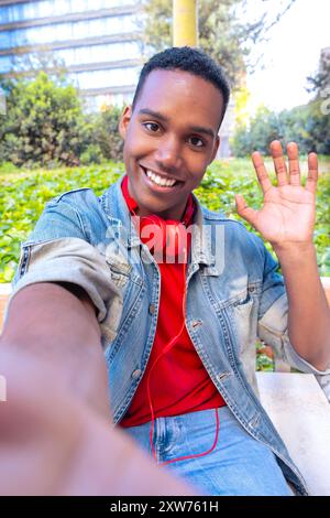 Uomo afroamericano che fa una videochiamata con il cellulare e sorride all'aperto. Foto Stock