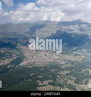 Panorama aereo panoramico della città, da un aereo da aliante, con il villaggio storico di Assergi e lo svincolo autostradale nelle vicinanze, girato da sud con una luminosa luce estiva Foto Stock